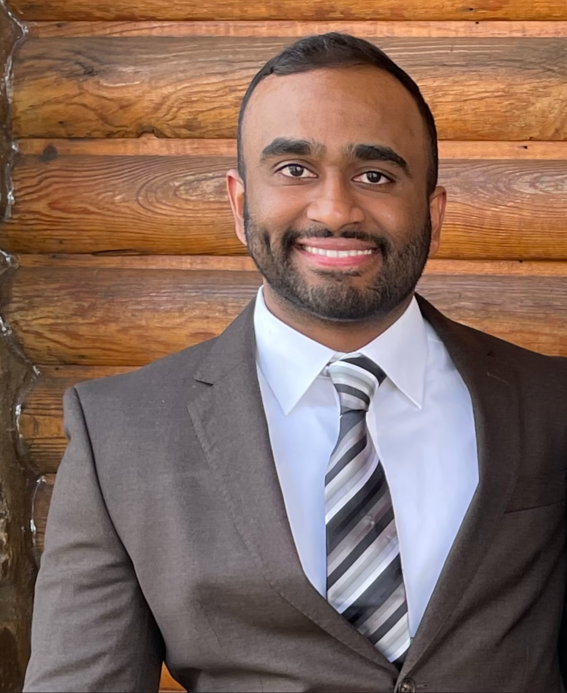 Kenneth Vaz smiling in a suit against a wooden wall